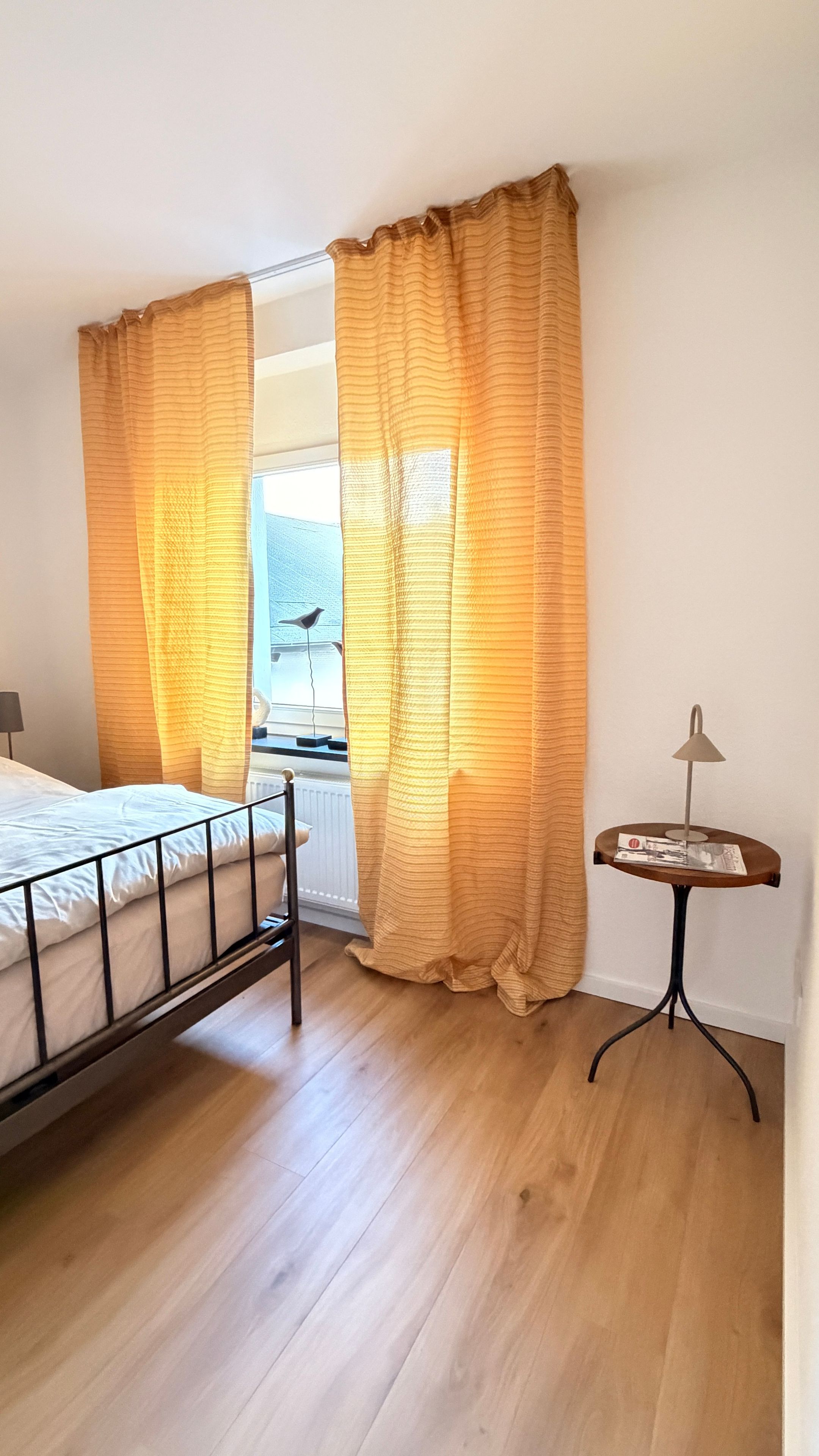 Ein Schlafzimmer mit einem Bett, einem kleinen Tisch und einem Fenster mit Vorhängen.