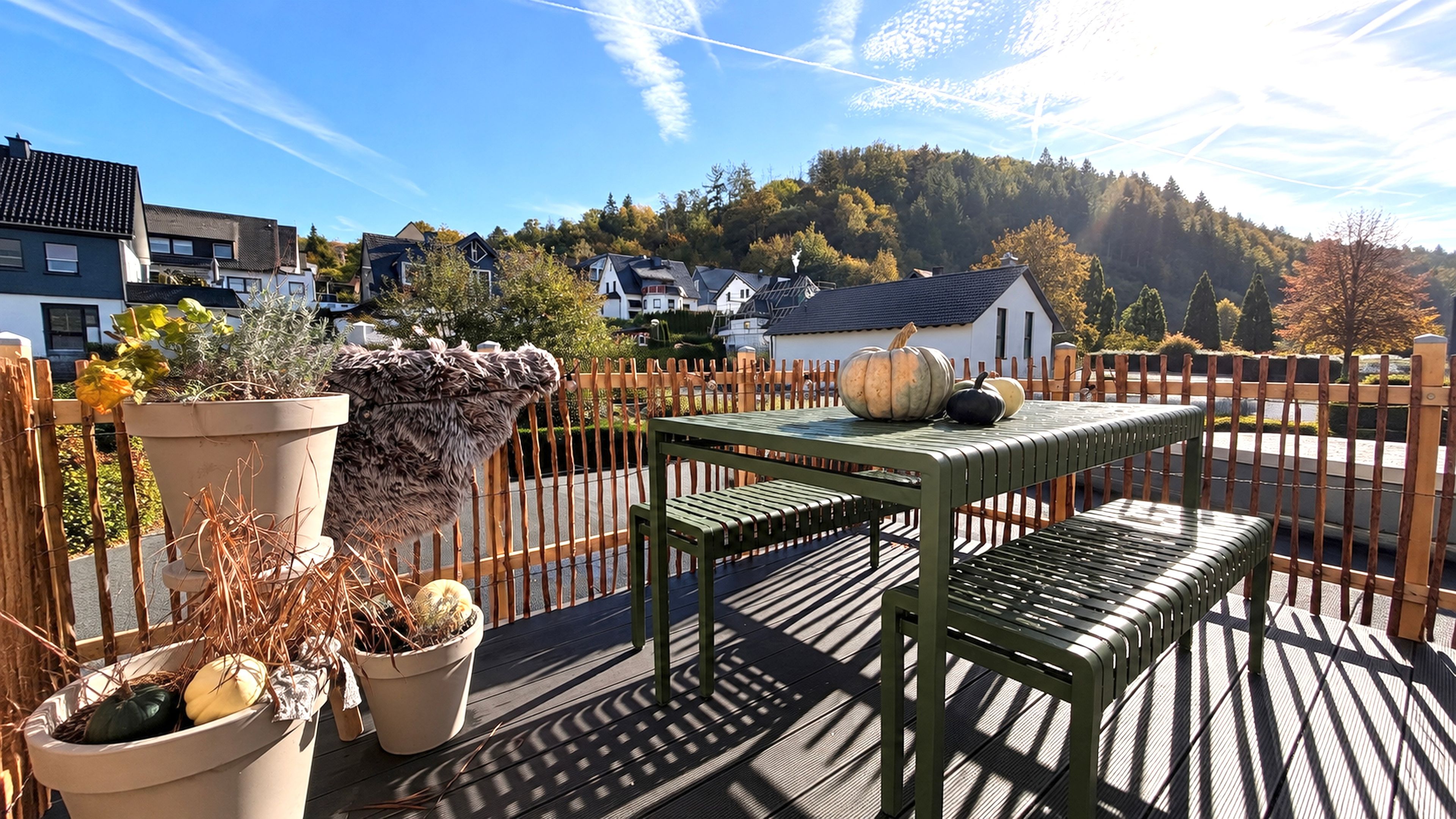 Eine Dachterrasse mit Tisch und Stühlen, Blumentöpfen und Blick auf Häuser und Bäume.