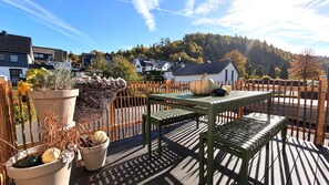 Eine Dachterrasse mit Tisch und Stühlen, Blumentöpfen und Blick auf Häuser und Bäume.
