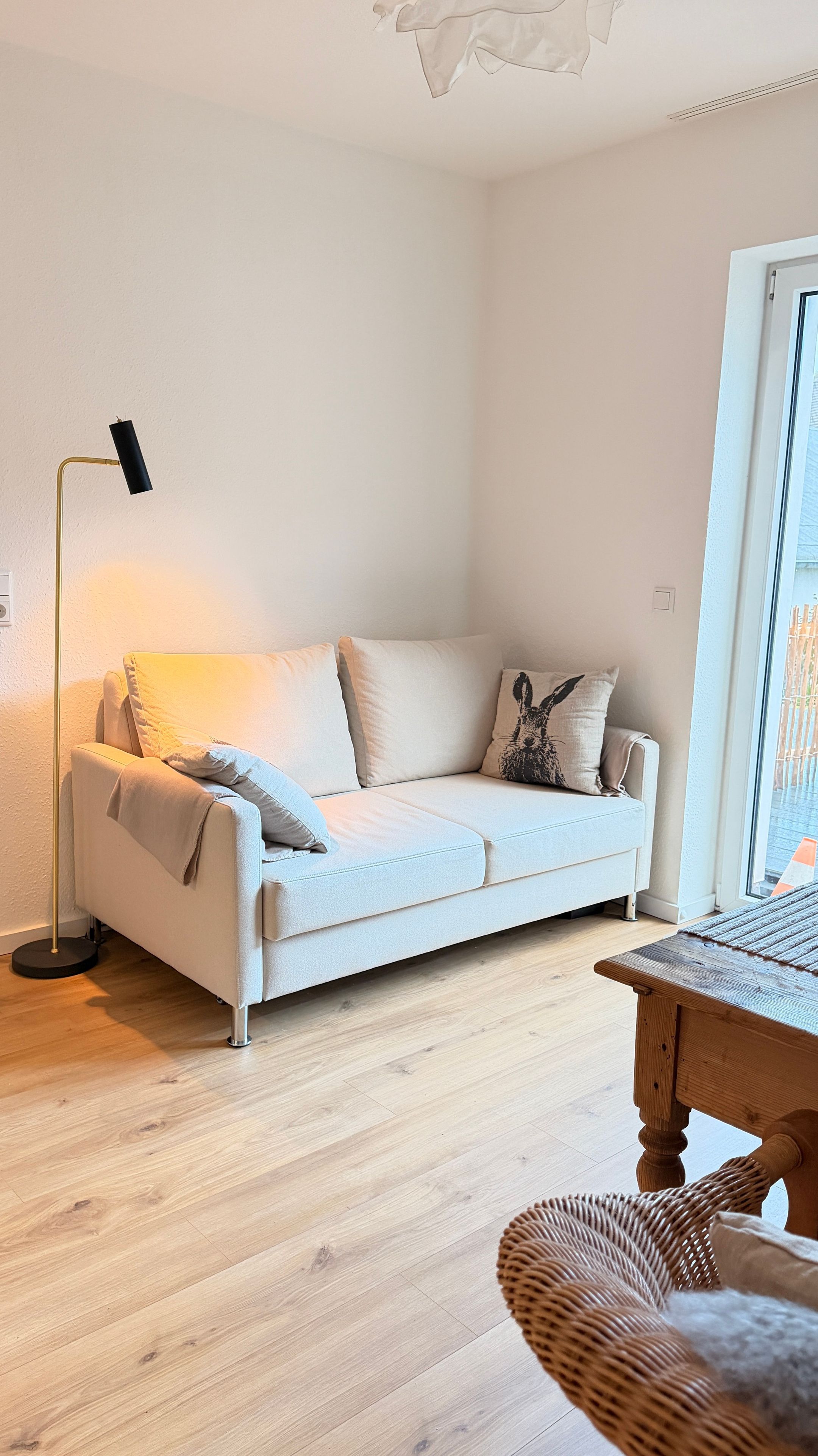 Ein modernes Wohnzimmer mit einem weißen Sofa, einer Stehlampe und einem Korbstuhl.