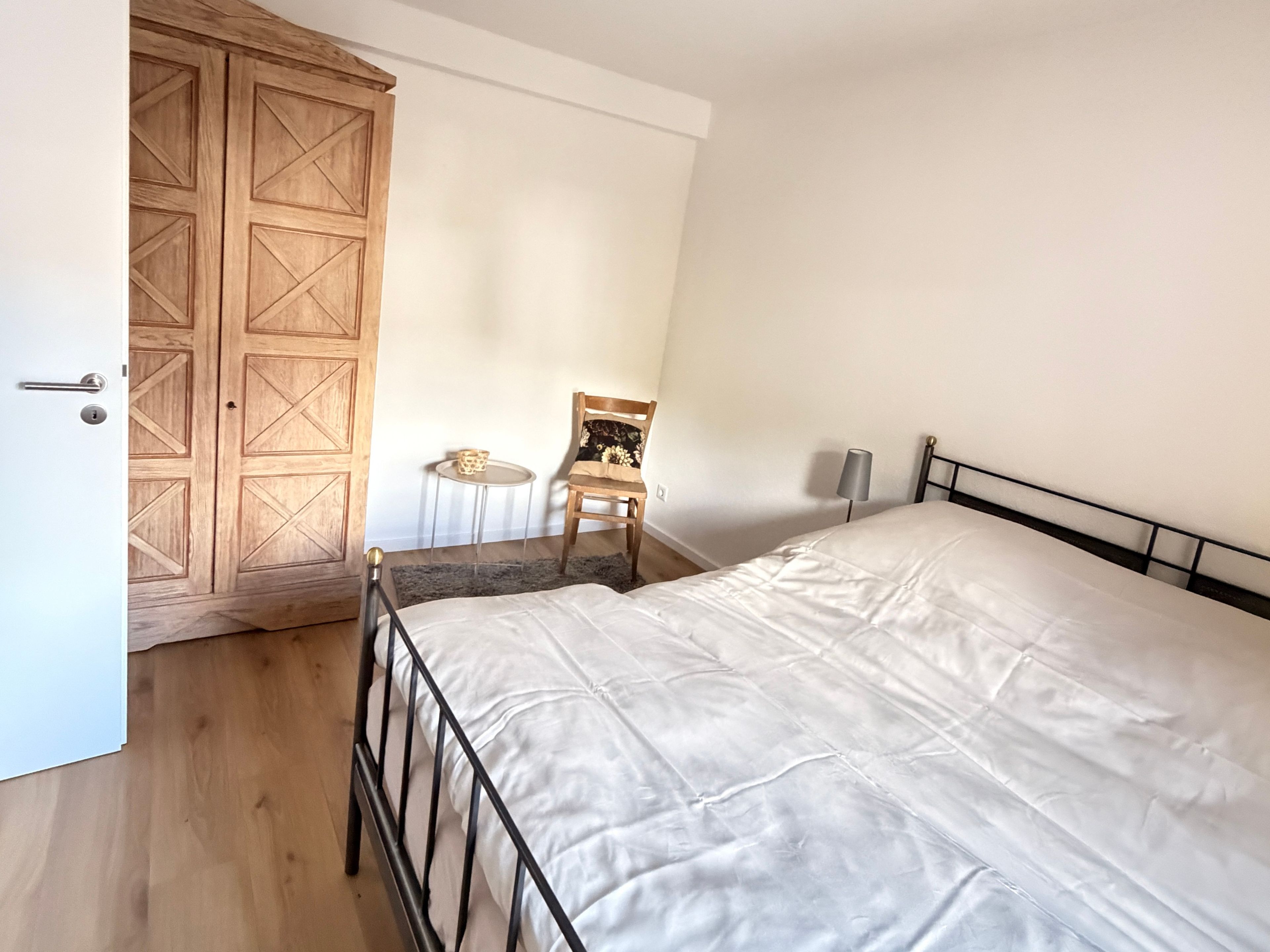 Ein Schlafzimmer mit einem Bett, einem Holzschrank, einem Sessel und einem kleinen Tisch.