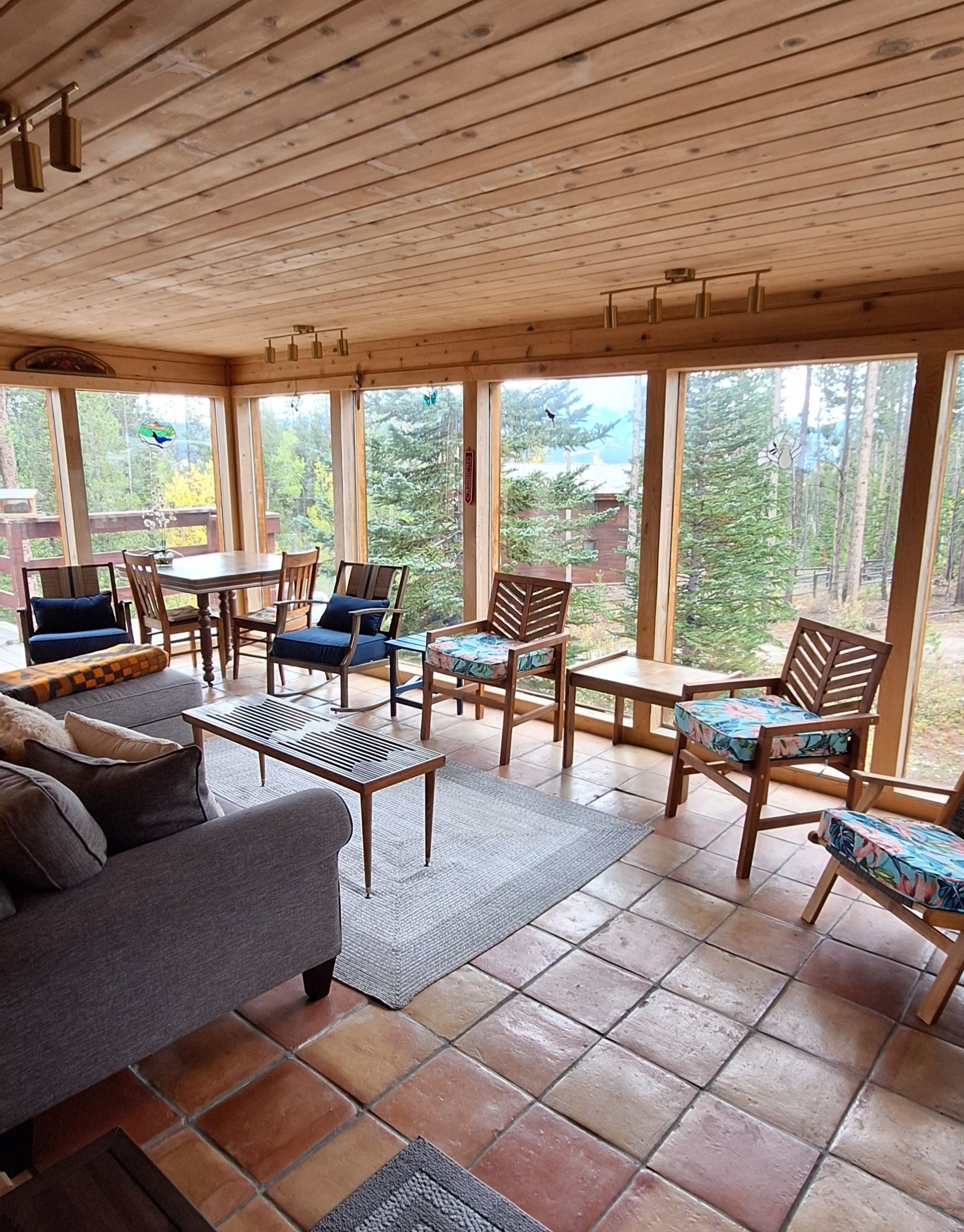 A wooden-paneled room with a sofa, chairs, and a table, large windows with a view of trees.