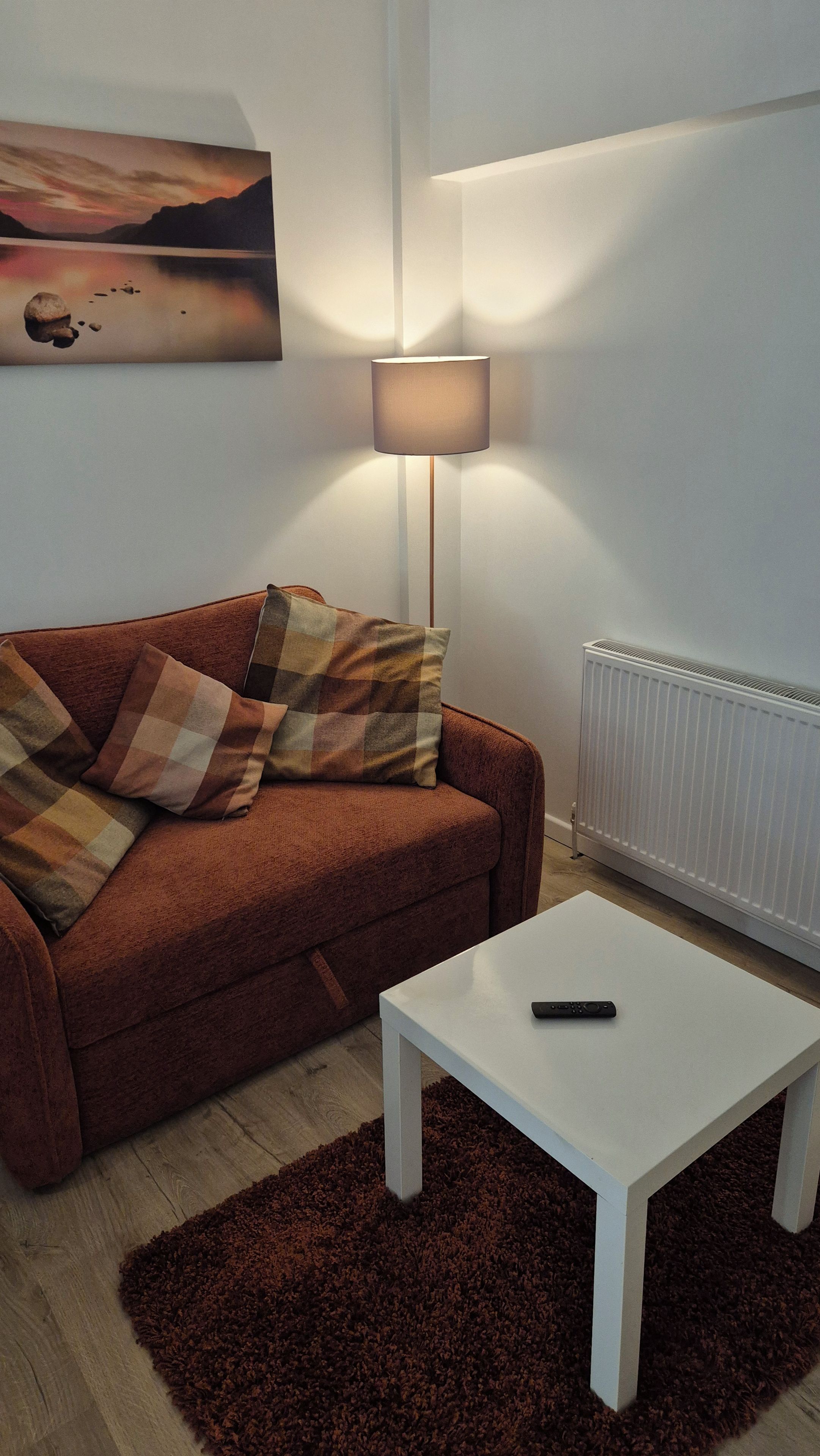 A living room with a brown sofa, white table, and a remote control on the table.