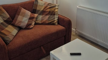 A living room with a brown sofa, white table, and a remote control on the table.
