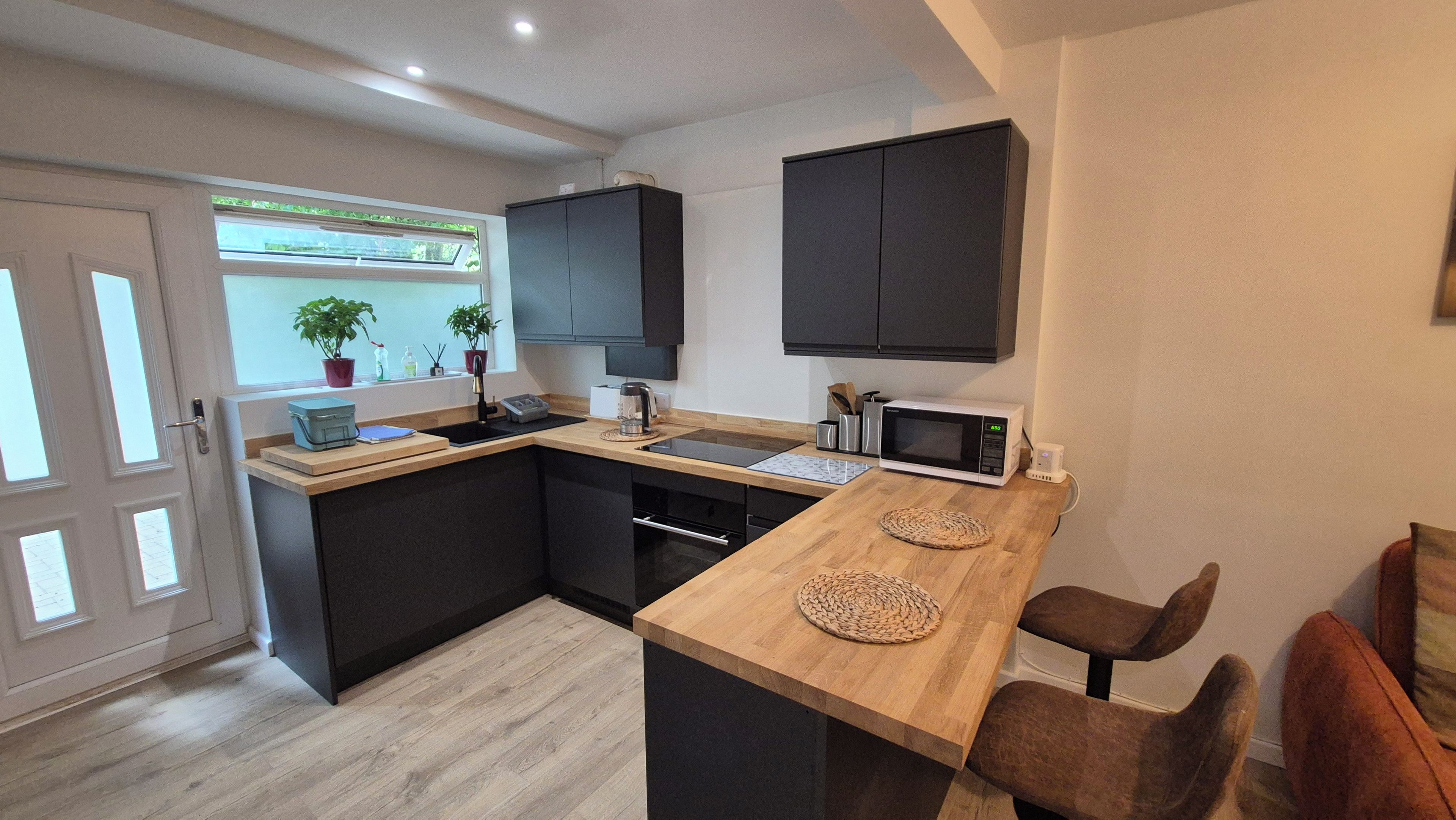 A modern kitchen with a wooden countertop, black cabinets, a microwave, and a sink.