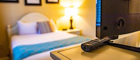 A hotel room with a bed, a bedside table with a remote control, and a lamp.