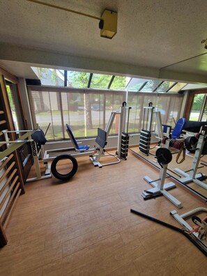 Un gimnasio con diverso equipamiento de ejercicio, amplias ventanas y piso de madera.