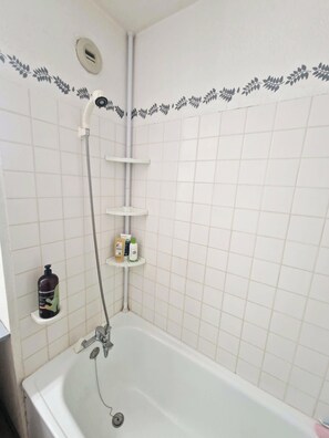 Un baño con bañera, ducha y estante con artículos de aseo.