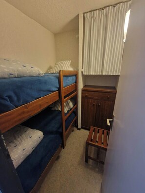 Una cama individual superpuesta con cabecera de madera, un mueble de madera pequeño y un taburete.