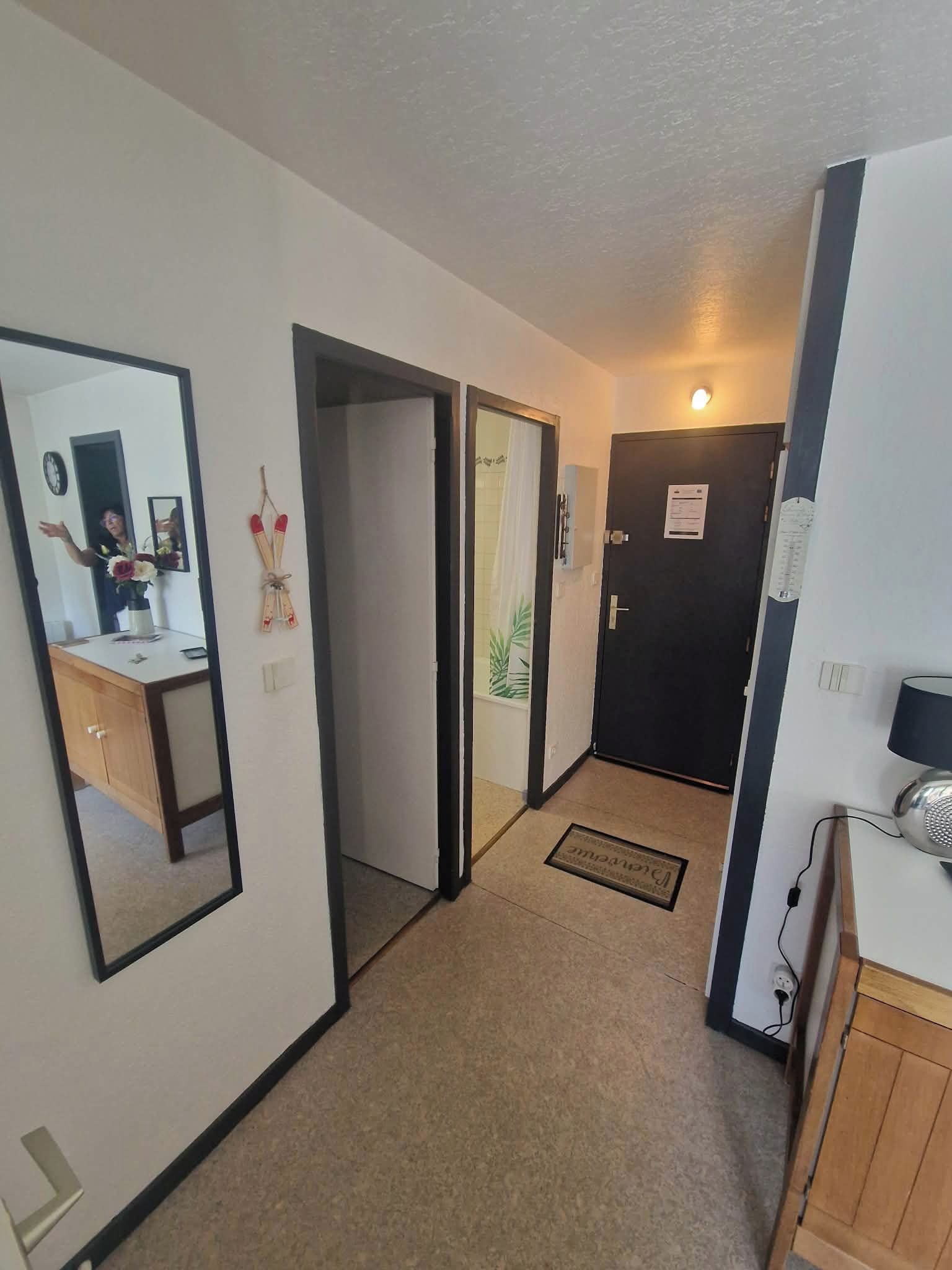 A hallway with a mirror, a door, and a small desk with a vase.