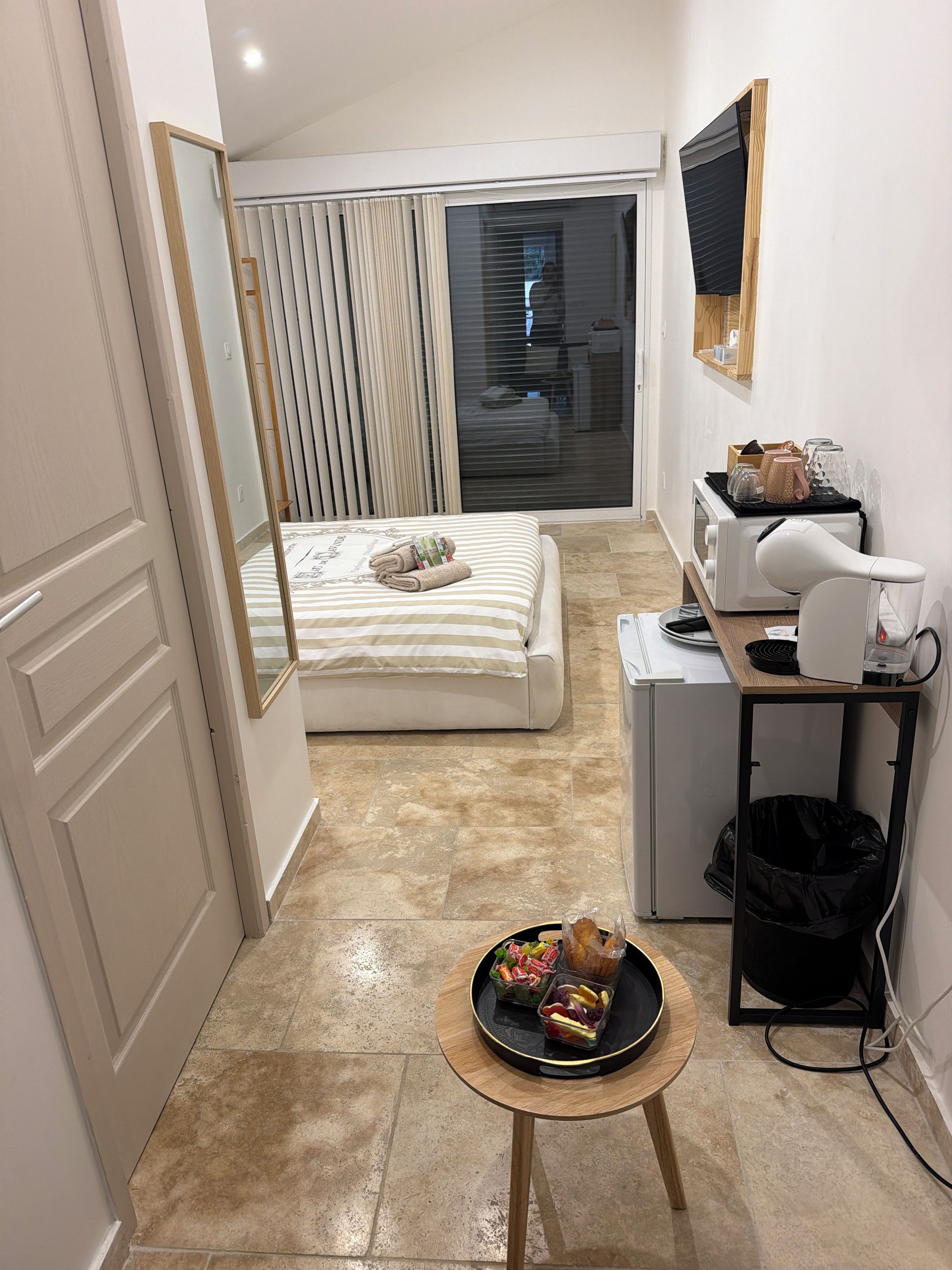 Een compacte hotelkamer met een bed, een klein keukentje, een aan de muur bevestigde televisie en een zithoek met een dienblad eten.