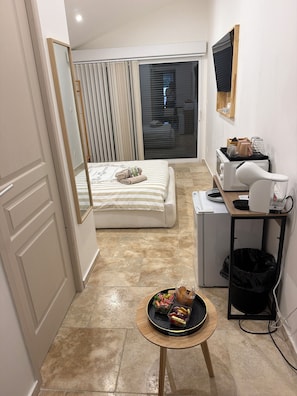 Een compacte hotelkamer met een bed, een klein keukentje, een aan de muur bevestigde televisie en een zithoek met een dienblad eten.