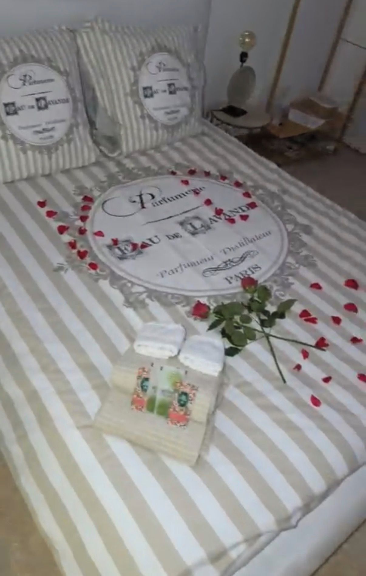 Een bed met een gestreepte spreidekker, een decoratief kussen, een klein fotolijstje en een boeket rode rozen.