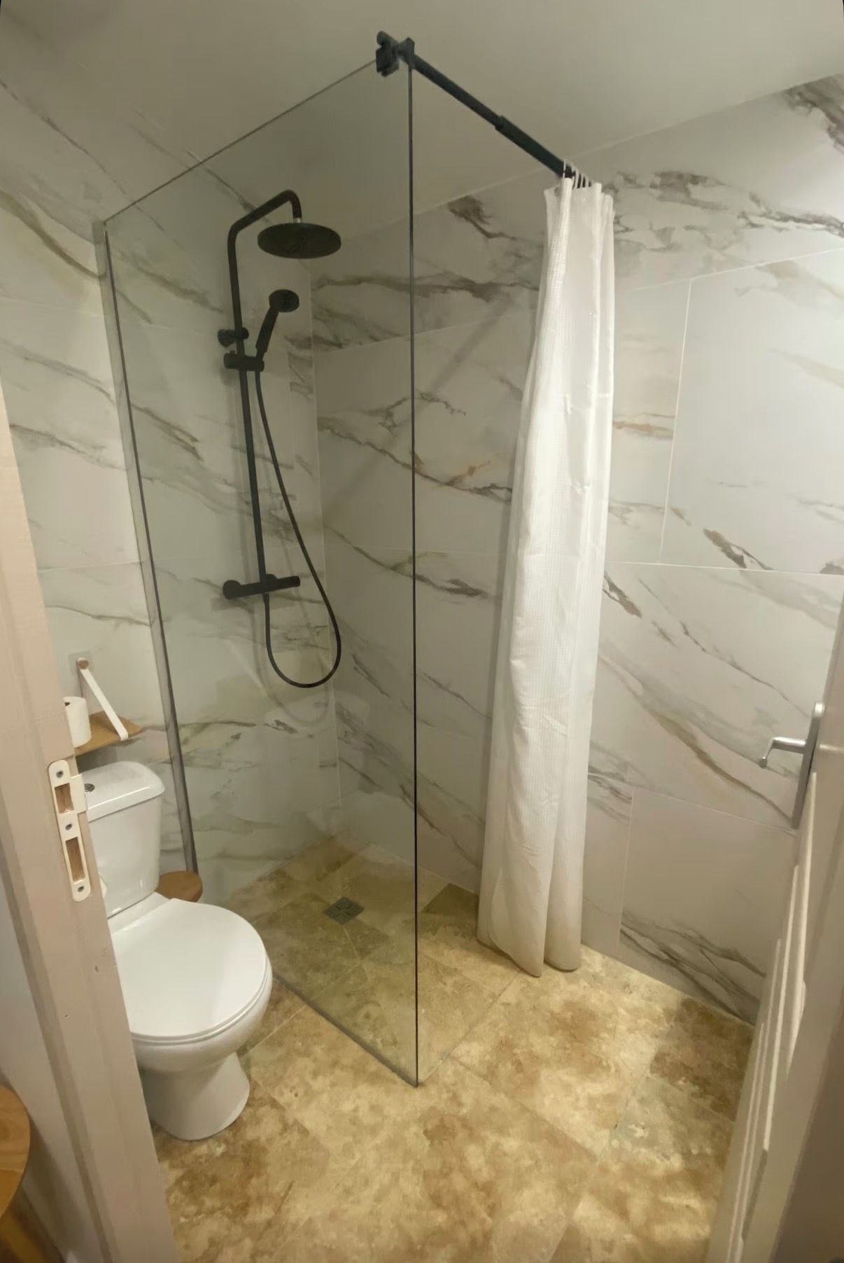 Een badkamer met een douchecabine van glas, toilet en wanden met een marmerlook.