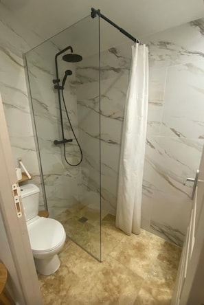 Een badkamer met een douchecabine van glas, toilet en wanden met een marmerlook.