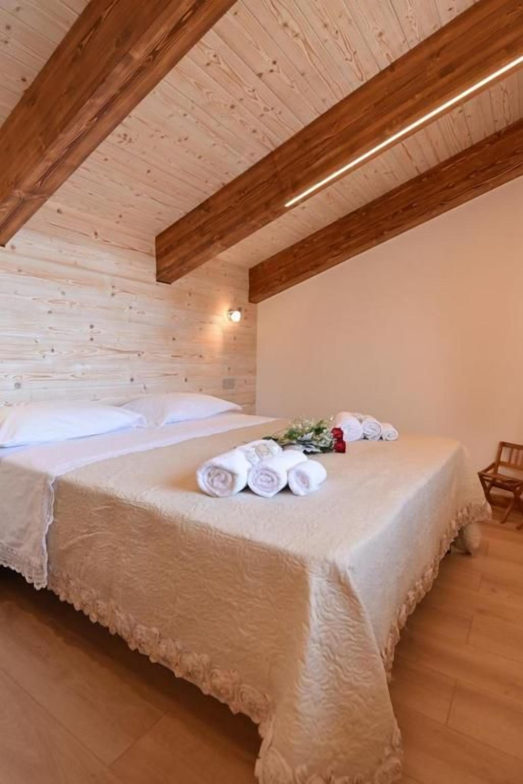A bedroom with a wooden ceiling, a bed with a white bedspread, and a small table with towels.