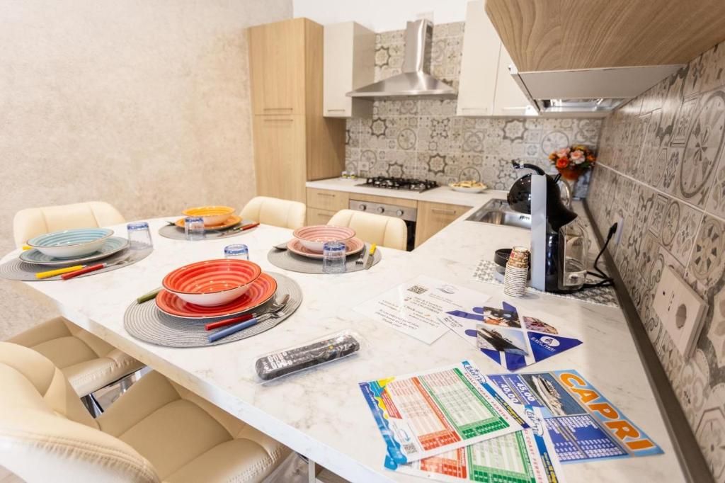 A kitchen with a marble countertop, a gas stove, and a sink. There are chairs around the table, and various kitchen items are scattered on the counter.
