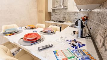 A kitchen with a marble countertop, a gas stove, and a sink. There are chairs around the table, and various kitchen items are scattered on the counter.