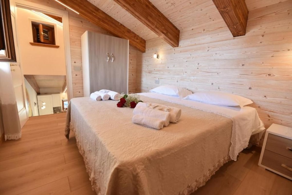 A bedroom with a large bed, wooden ceiling beams, a wardrobe, and a bedside table.