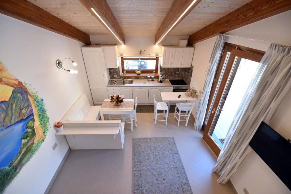 Cocina compacta con armarios blancos, comedor con mesa y sillas, y un ventanal con cortinas.