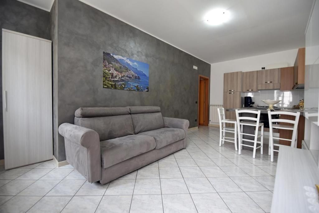 Un salon avec un canapé gris, un coin repas avec des chaises blanches et une cuisine avec des meubles en bois.