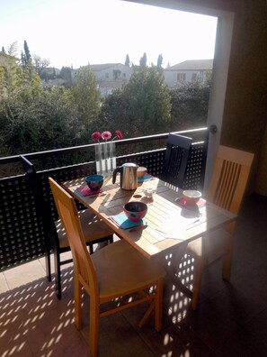 Uma varanda com mesa, cadeiras e vista para edifícios e árvores.