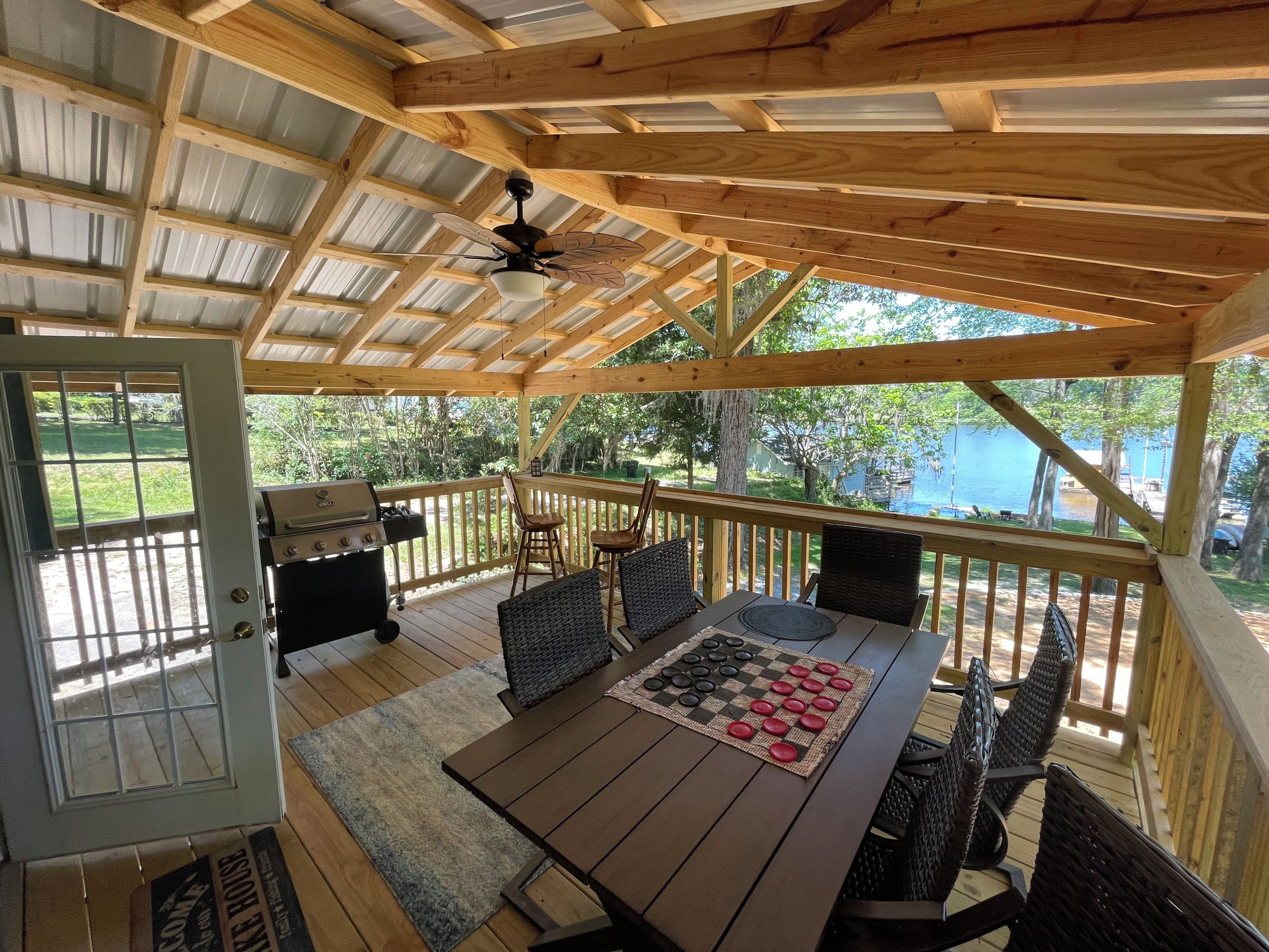 A covered outdoor deck with a table and chairs, a ceiling fan, and a view of a lake.