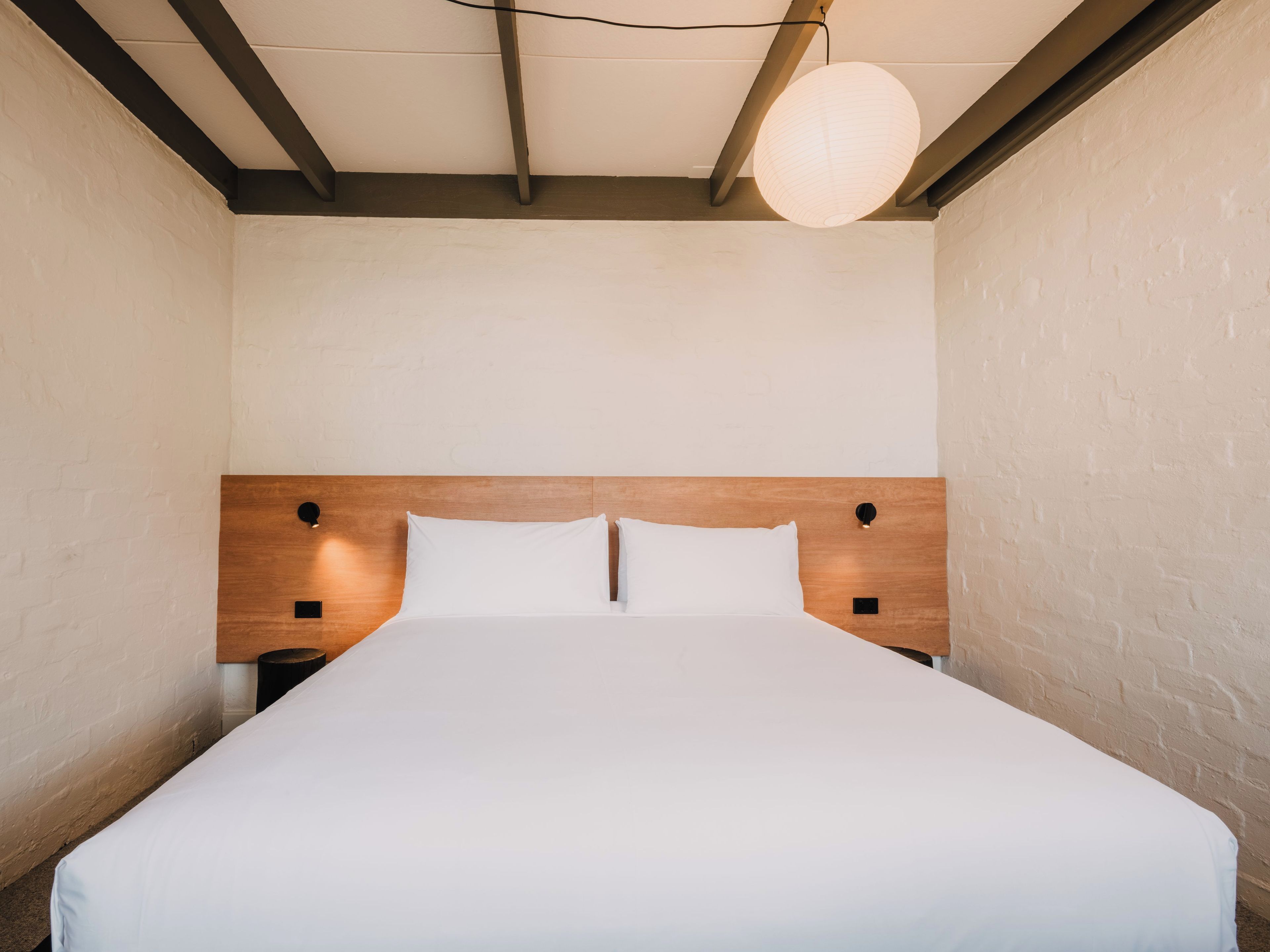 Habitación de hotel con cabecera de madera, dos mesitas de noche y una cama individual con ropa blanca.