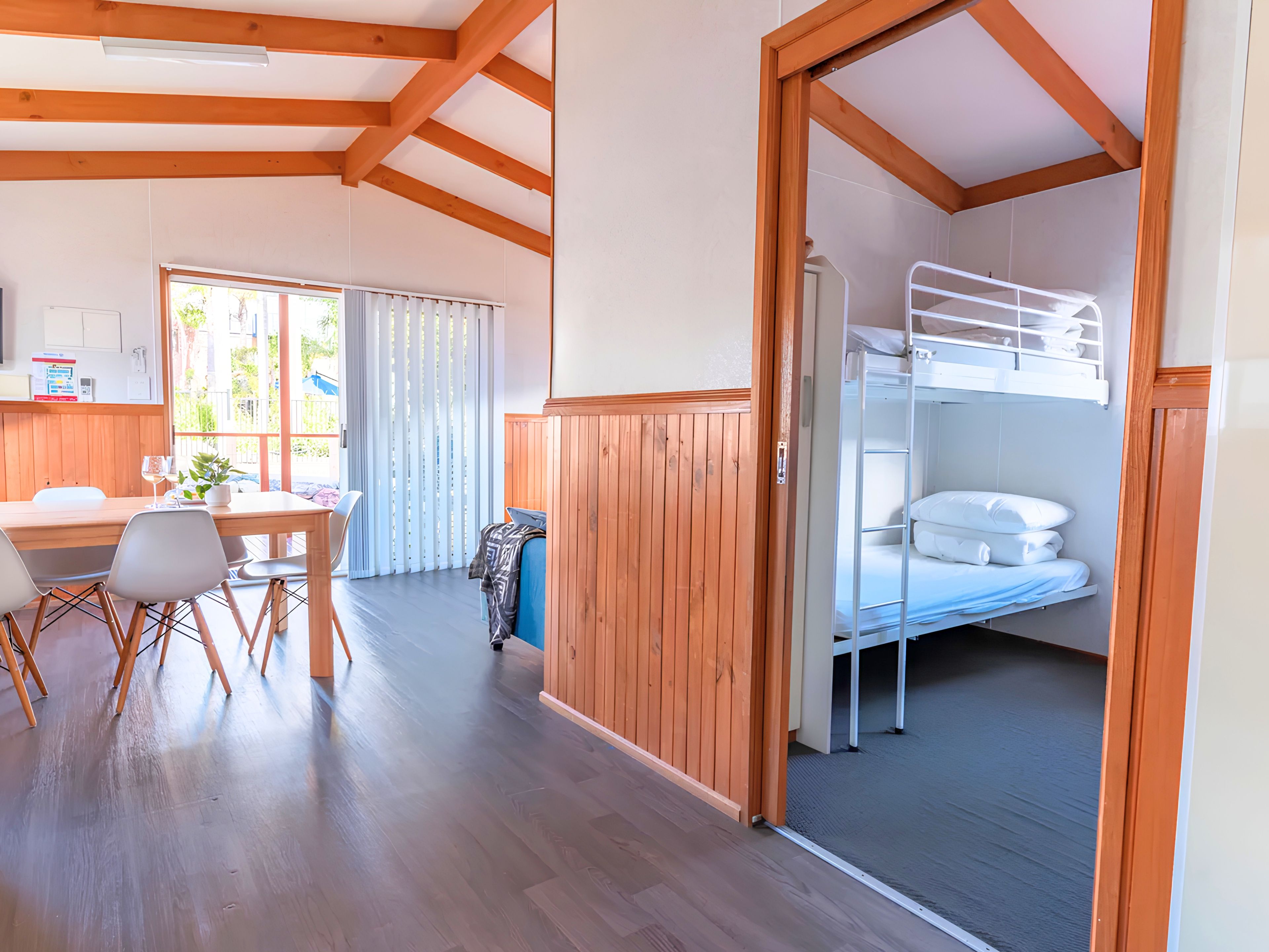 Een kamer met een stapelbed, een eethoek met een tafel en stoelen, en uitzicht door een raam.