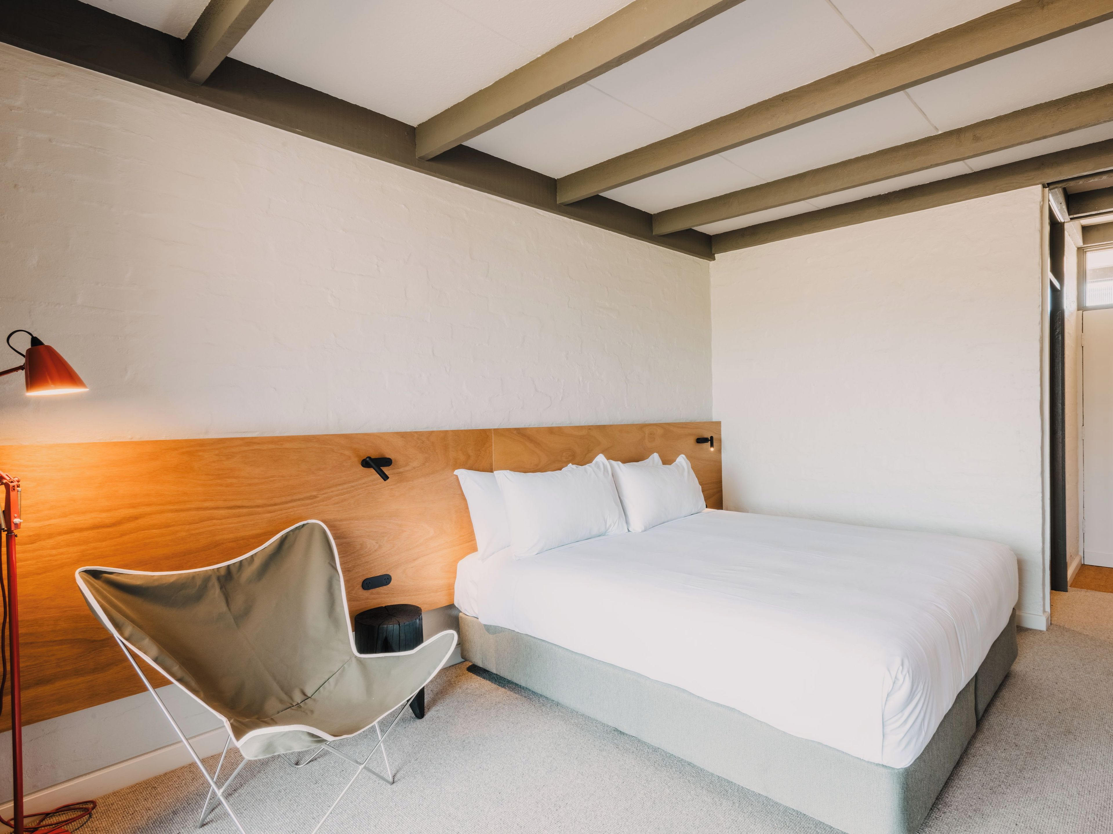 Un dormitorio con cama, una silla, una lámpara y un cabecero de madera.