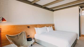 Un dormitorio con cama, una silla, una lámpara y un cabecero de madera.