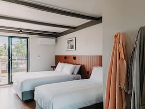 A hotel room with two beds, a sliding glass door to the outside, a framed picture on the wall, and a coat rack with a striped towel. - The Black Dolphin Holiday Park (Merimbula)
