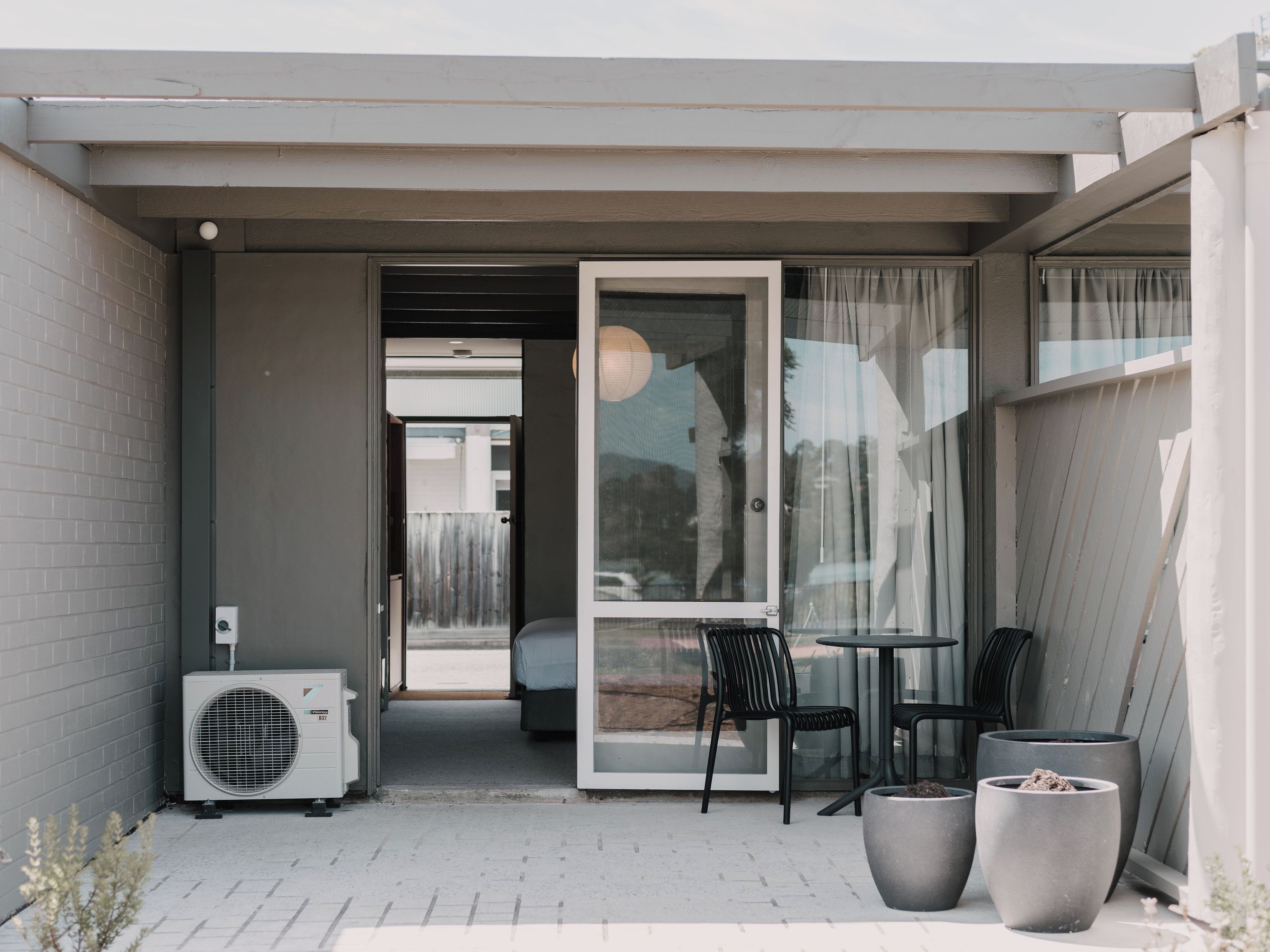 Un espace extérieur aménagé avec une table et des chaises, une plante en pot et un appareil de climatisation.