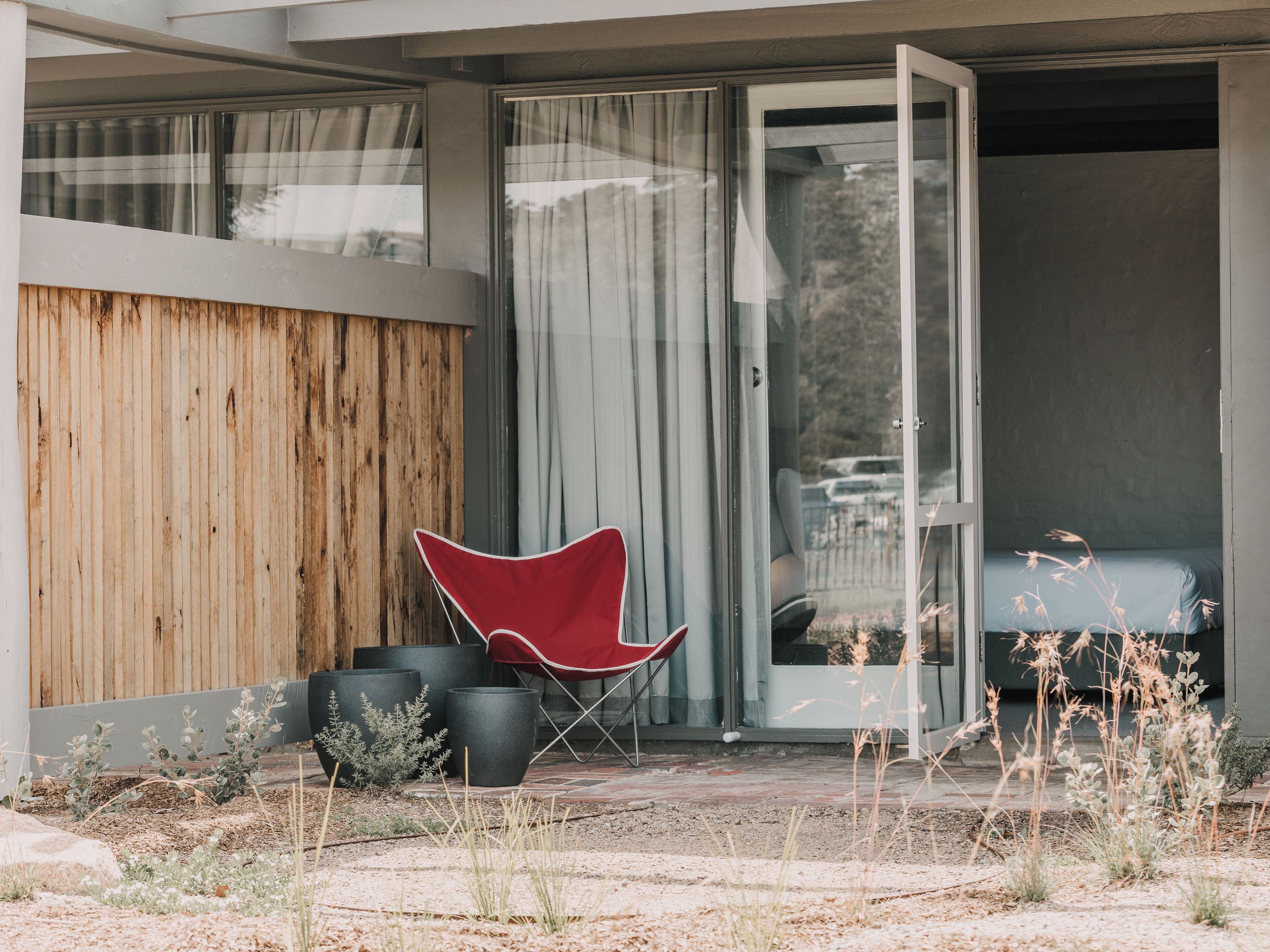Un espacio al aire libre moderno con una silla roja, macetas negras y un muro de madera.