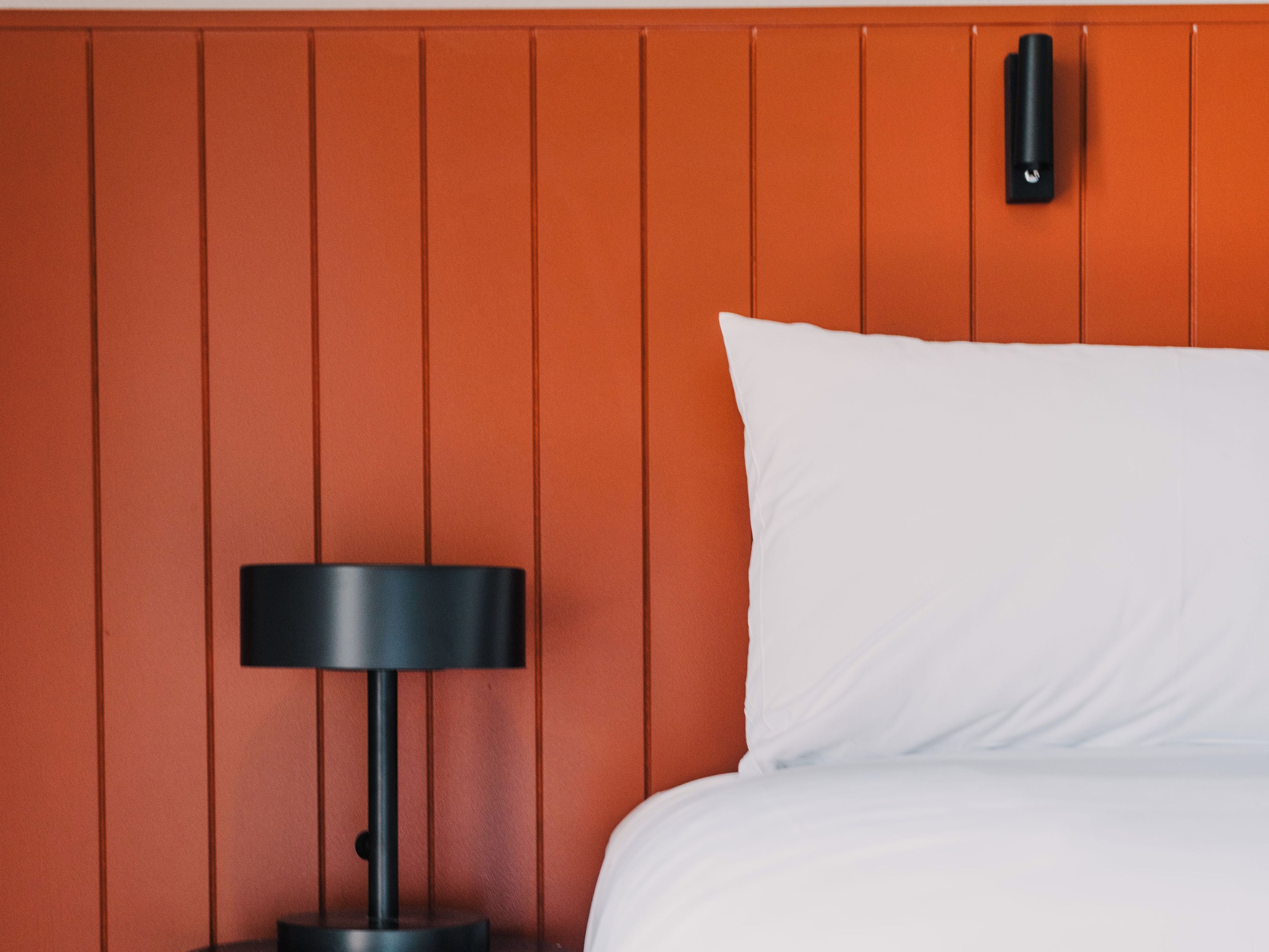 A bed with white bedding against a wall with vertical paneling.