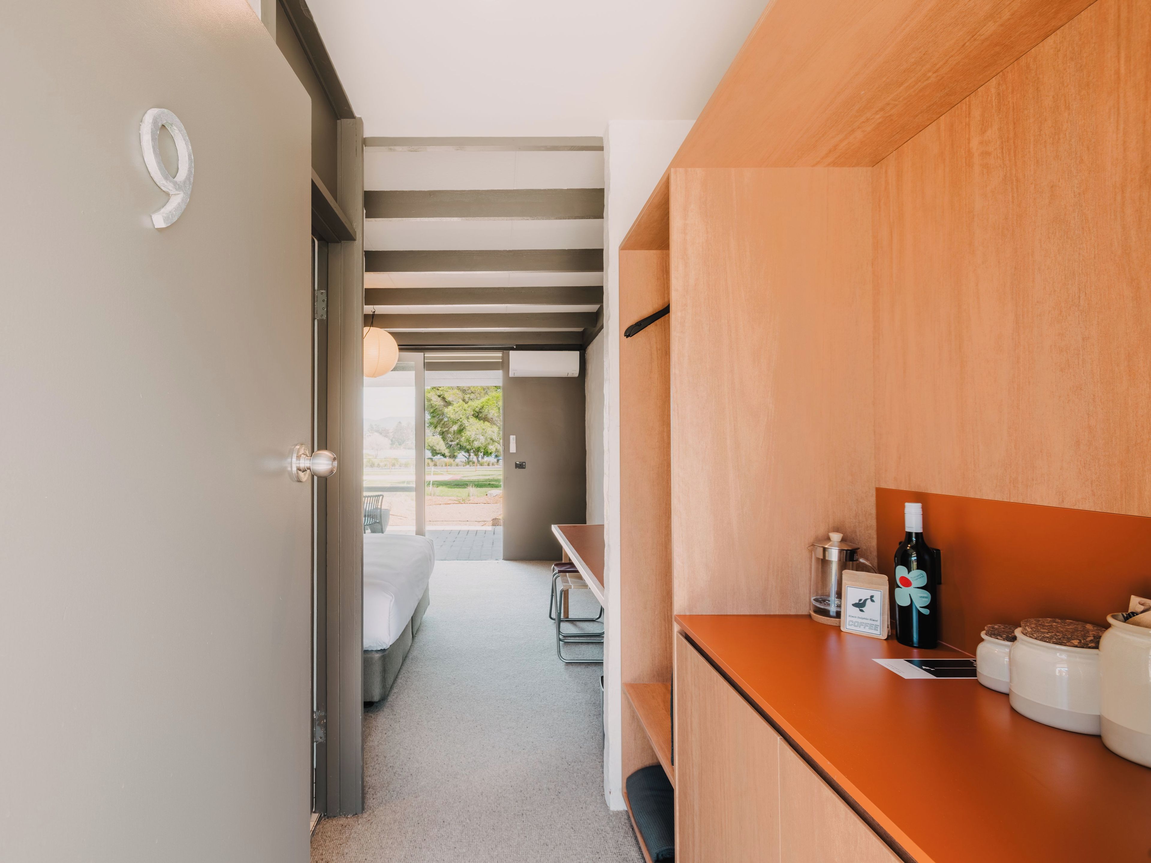 A modern kitchen with a wooden countertop, a sink, and a view of a garden through an open door.