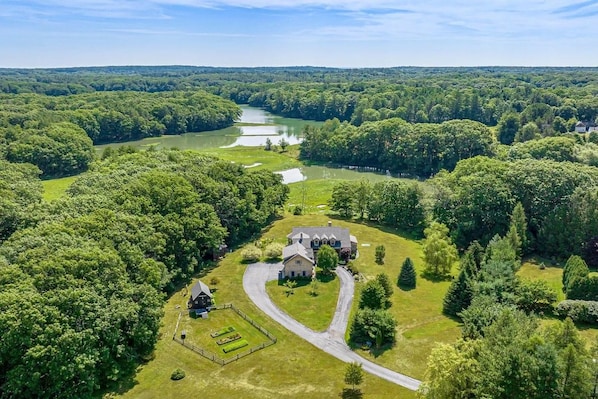 Un vaste domaine comprenant une maison principale, un étang et une pelouse bien entretenue.