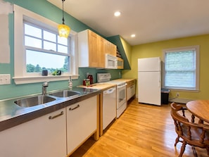 A compact kitchen with a sink, microwave, and oven, wooden cabinets, and a dining area with a table and chairs. - Spacious 4BR/4BA York Retreat w/ Big Backyard (York)
