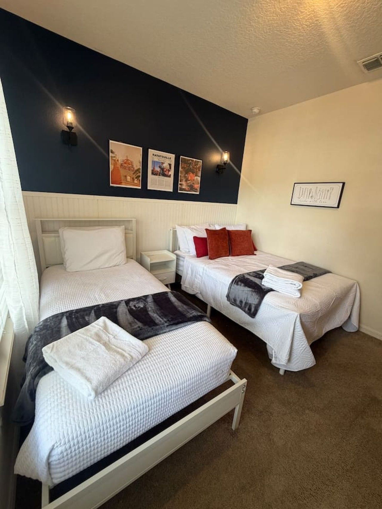 A hotel room with two beds, a nightstand, and wall-mounted light fixtures.