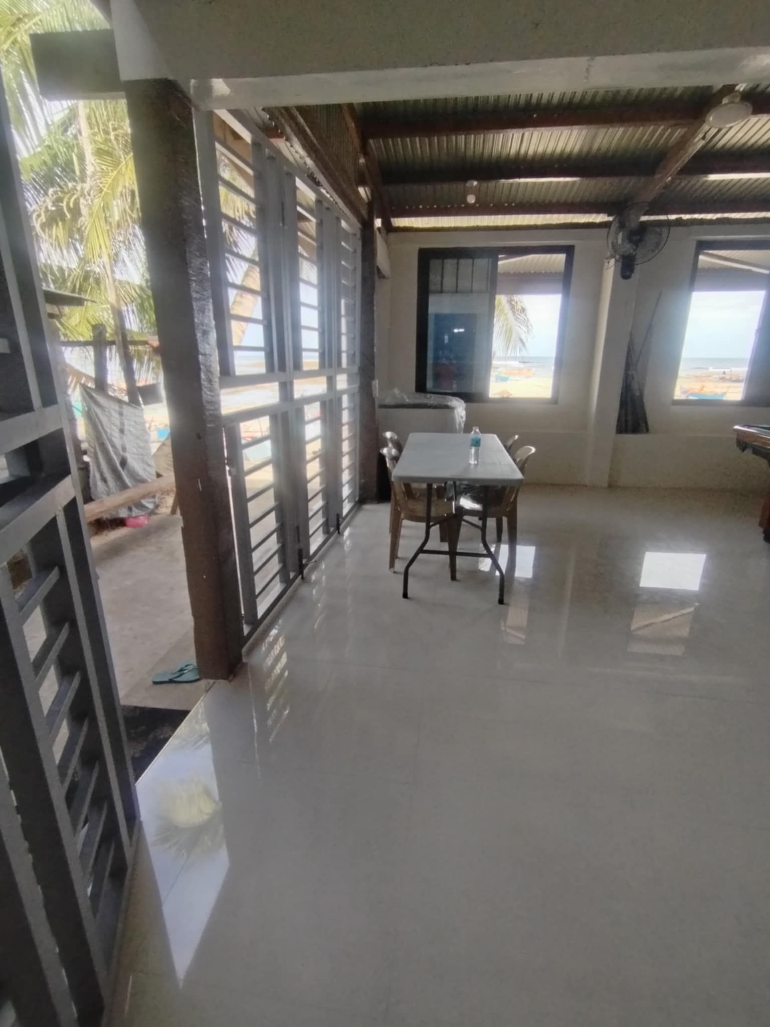 Una habitación con una mesa y sillas, una ventana con vista a la playa y una reja de metal.
