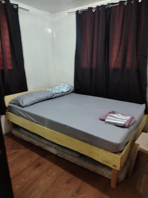 A single bed with a grey mattress and pillows, a wooden frame, and black curtains. - GUMOBAO STAYCATION HOUSE (Baganga)