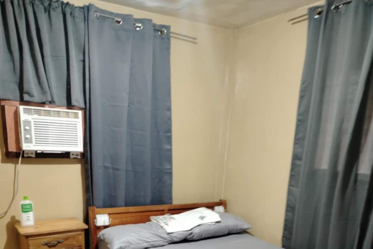 A single bed with a wooden frame, a bedside table with a bottle, and a wall-mounted heater.