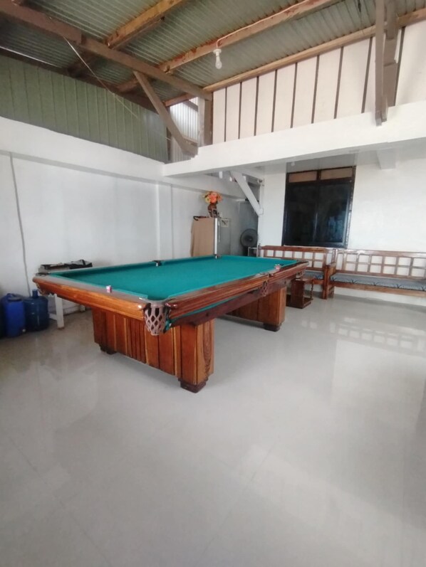 A pool table in a room with a high ceiling and a window.