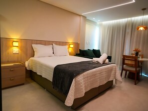 A modern hotel room with a large bed, bedside tables, a desk with a chair, and a window with curtains. - New Listing (Salvador)