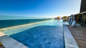 A swimming pool with a clear view of the ocean, a wooden deck, and a glass barrier. - New Listing (Salvador)