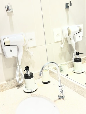 A bathroom with a sink, a mirror, a hairdryer, and a bottle of hand soap. - New Listing (Salvador)