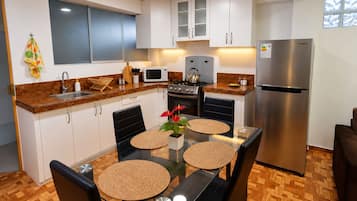 A modern kitchen with white cabinets, stainless steel appliances, and a glass dining table with woven placemats.