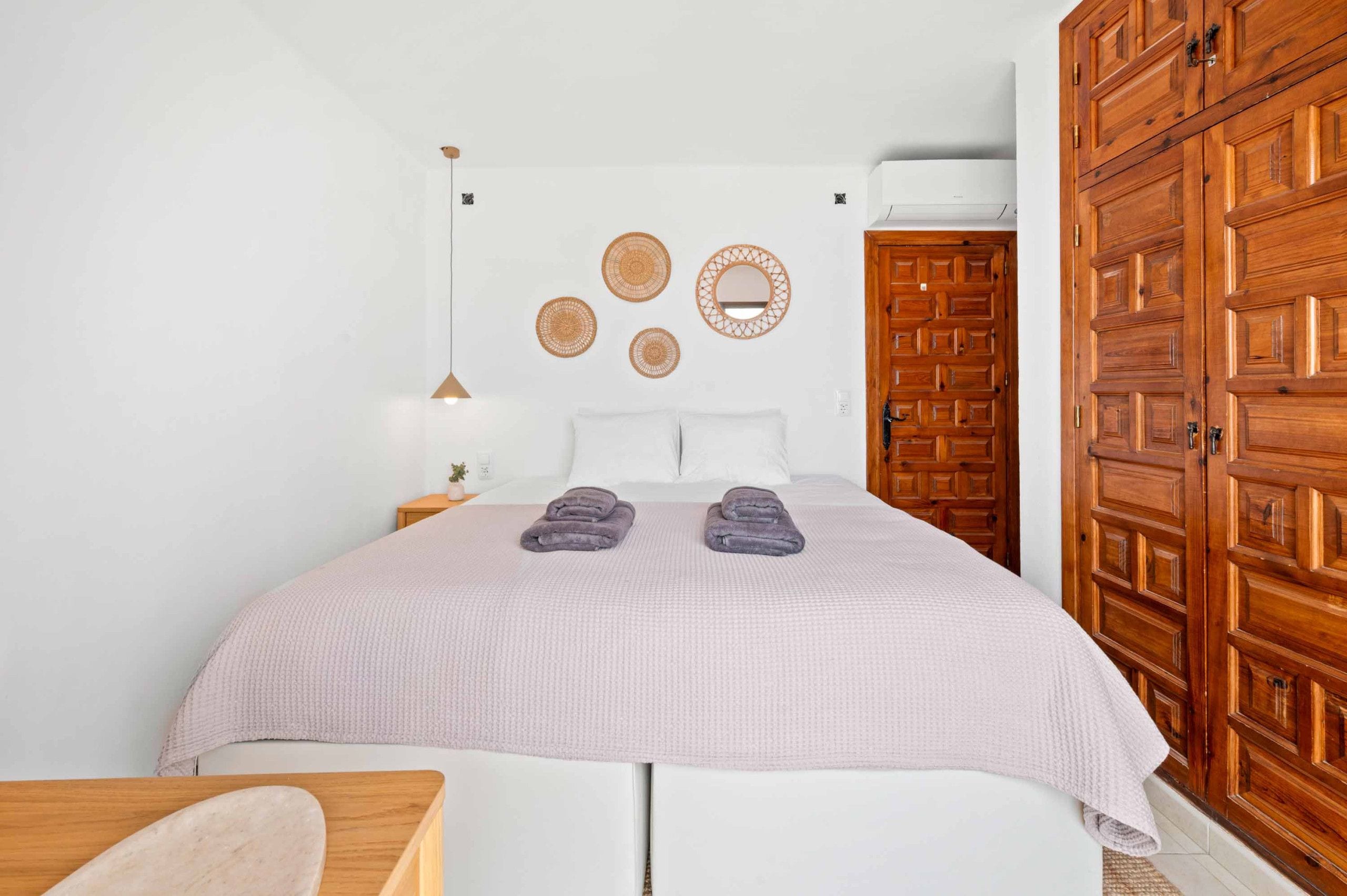 A bedroom with a bed, two wall-mounted circular mirrors, a wooden wardrobe, and a small bedside table with a lamp.