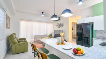 A modern kitchen with a central island, dining area with chairs, and a sofa.