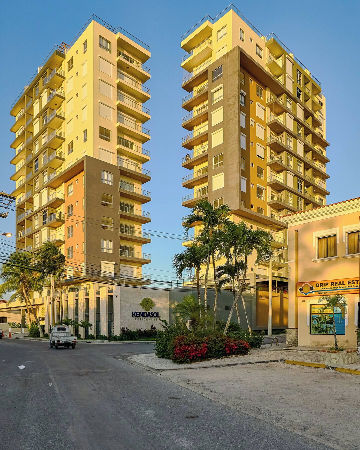 A high-rise residential building with multiple balconies, a sign for 'Kendasol Residences', and a parked vehicle in front.